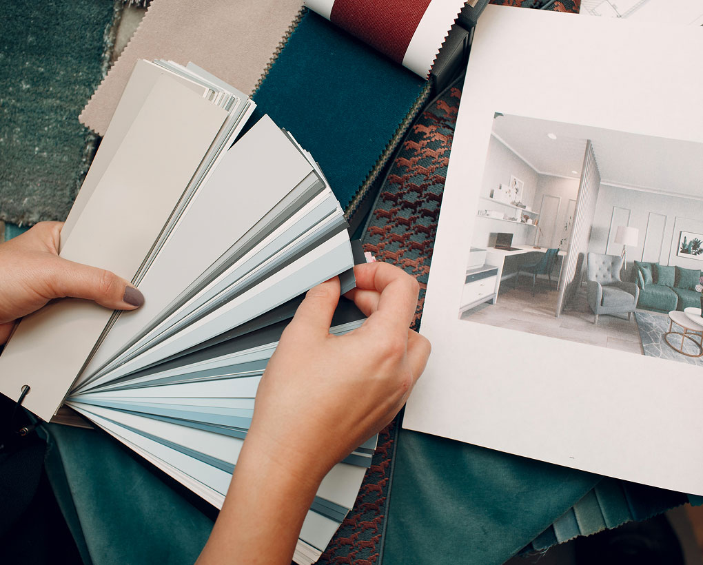 Persona che sfoglia una serie di campioni di colori, con un progetto di interni e tessuti sullo sfondo.